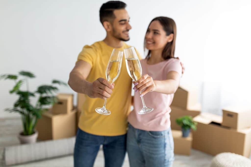 Happy couple celebrating their new home with champagne after moving in, surrounded by boxes — symbolising the joy of buying a property in Australia.